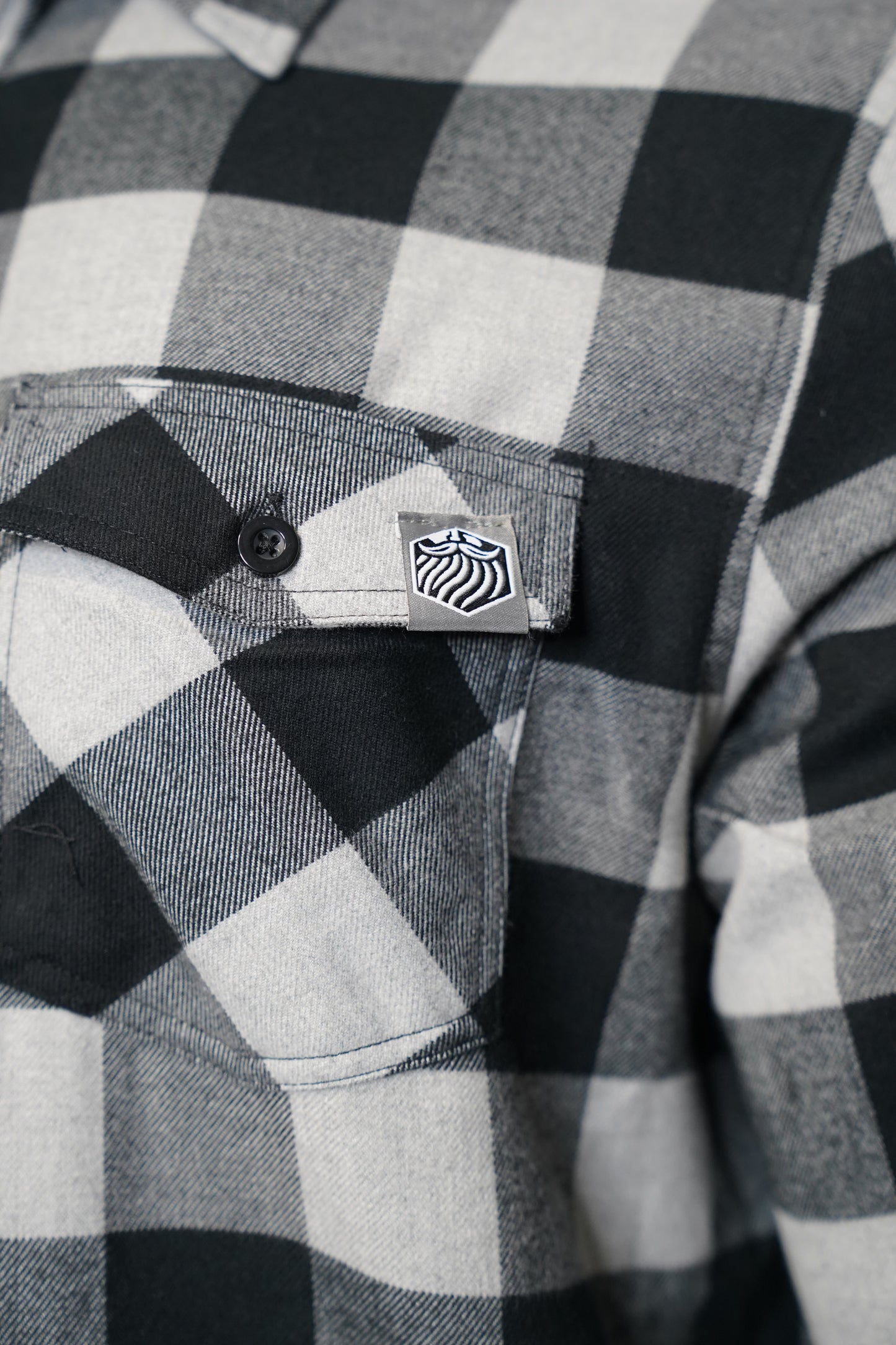 Close-up of a black and white checkered shirt with a brand logo on the chest pocket.