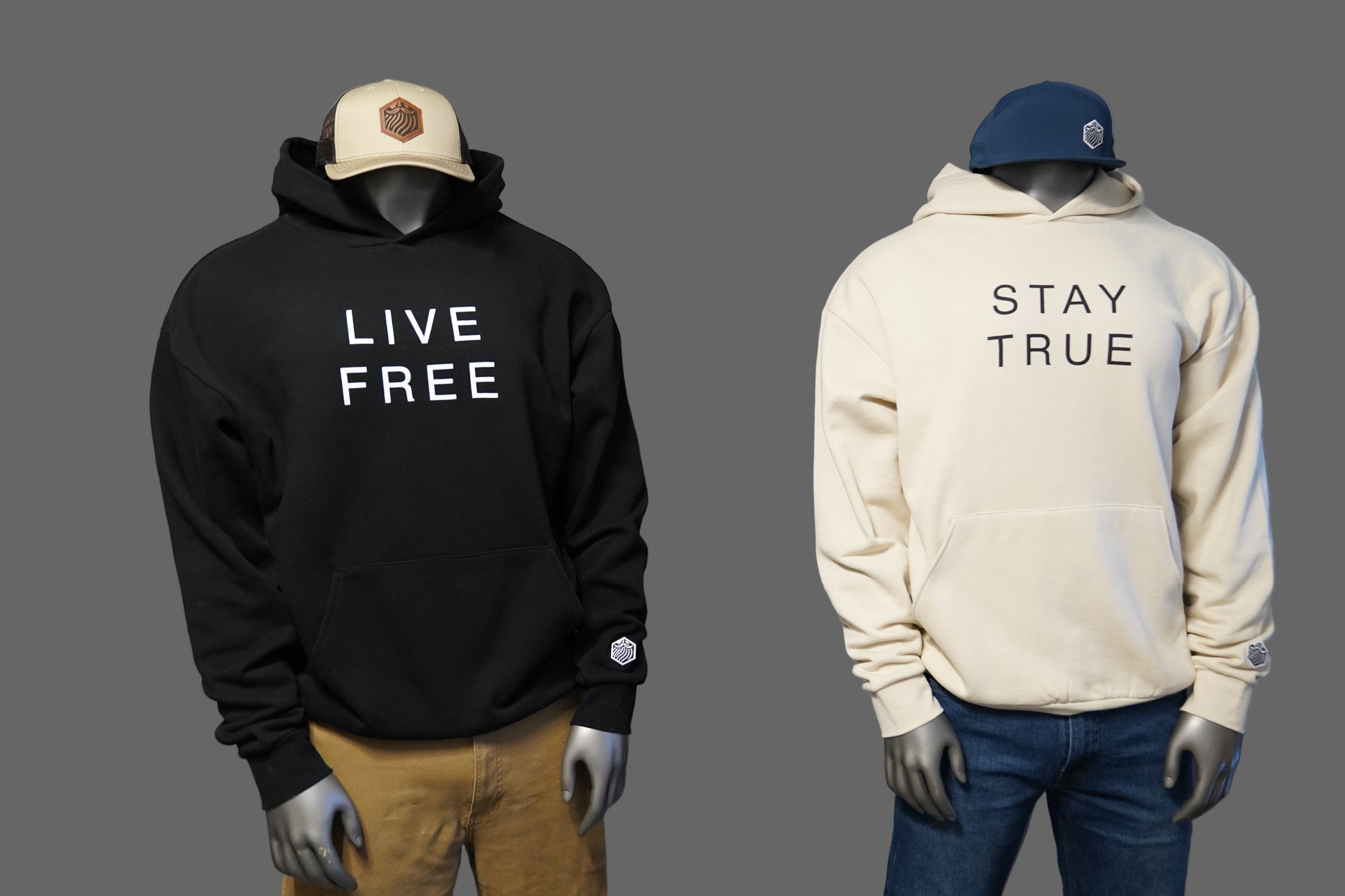 Two hoodies, one black with 'Live Free' text and one ivory with 'Stay True' text,  against a gray background.